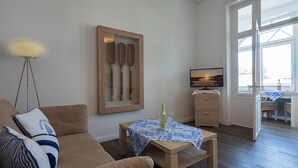 Ein Wohnzimmer mit einer Couch, einem Couchtisch, einem Bilderrahmen mit Paddeln, einem Fernseher und Blick durch ein Fenster.