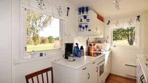 A kitchen with white cabinetry, a wooden chair, a window with a view of trees, and a shelf with blue and green glassware. - Amazing home in årjäng with WiFi (Årjäng)