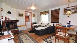 A cozy living room with a fireplace, a sofa, a dining table with chairs, and a patterned rug. - Amazing home in årjäng with WiFi (Årjäng)
