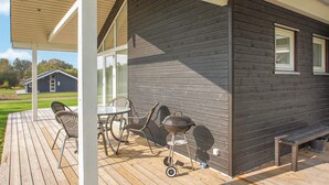 Een houten terras met een barbecue, stoelen en een tafel.