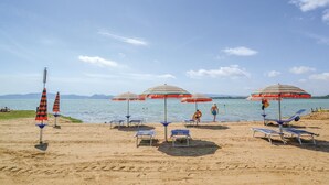 A beach with striped umbrellas, sun loungers, and a clear view of the water. - Pet friendly apartment in Castiglion del Lago PG with outdoor swimming pool (Castiglion del Lago PG)