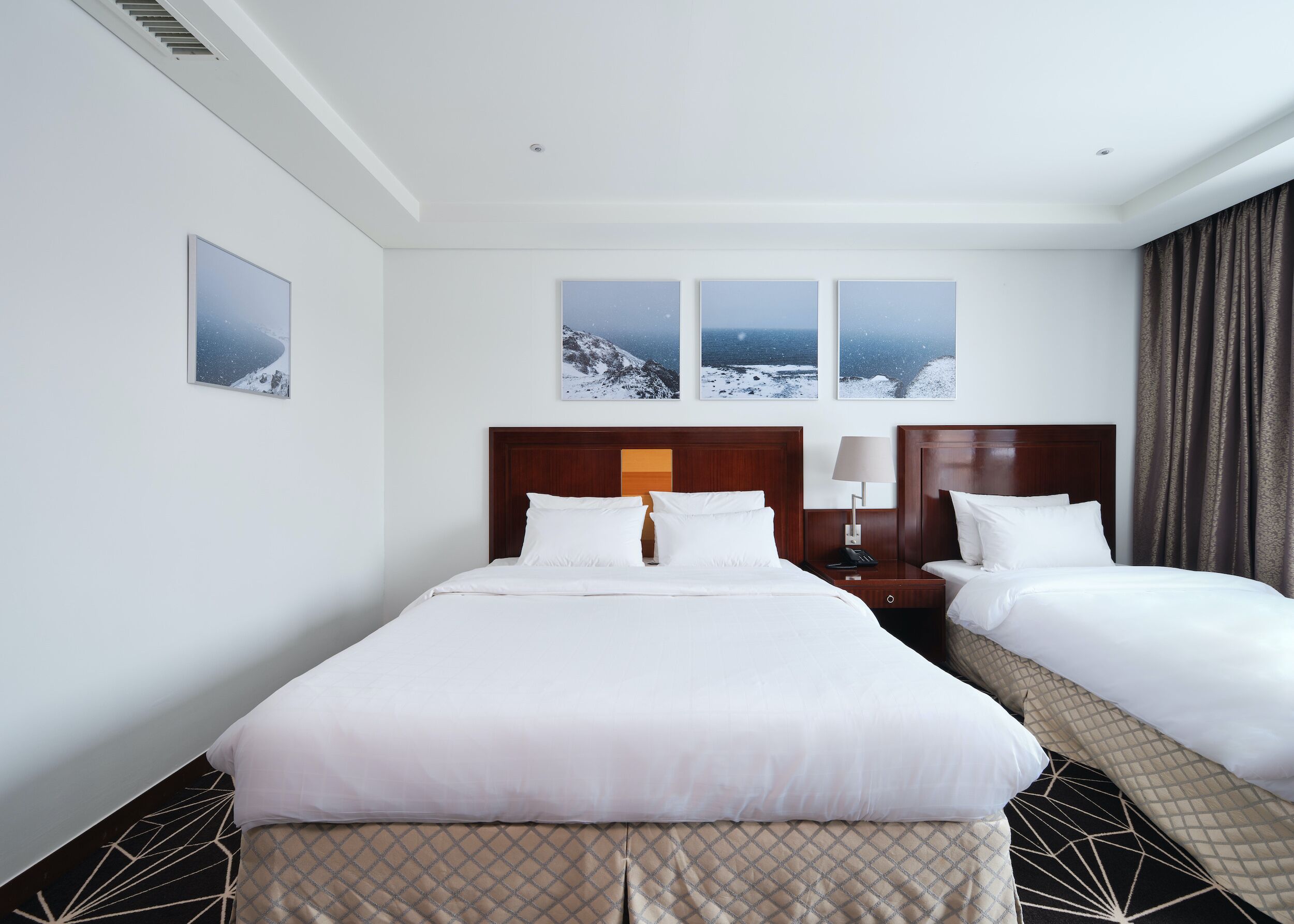 Ein Hotelzimmer mit einem großen Bett, zwei Nachttischen, einem Beistelltisch und drei gerahmten Bildern an der Wand.