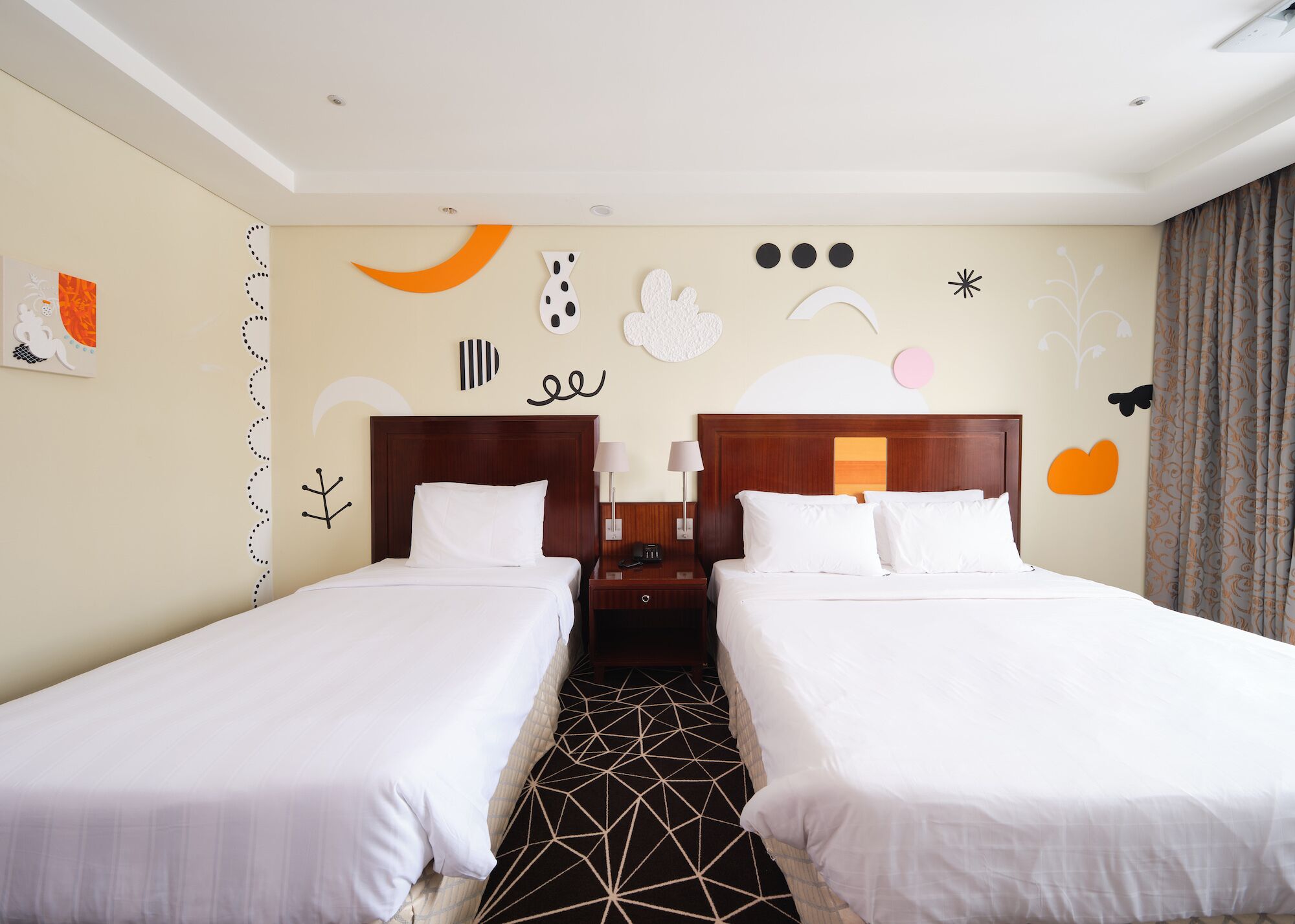 A hotel room with two beds, a nightstand, a wall clock, and a window with curtains.