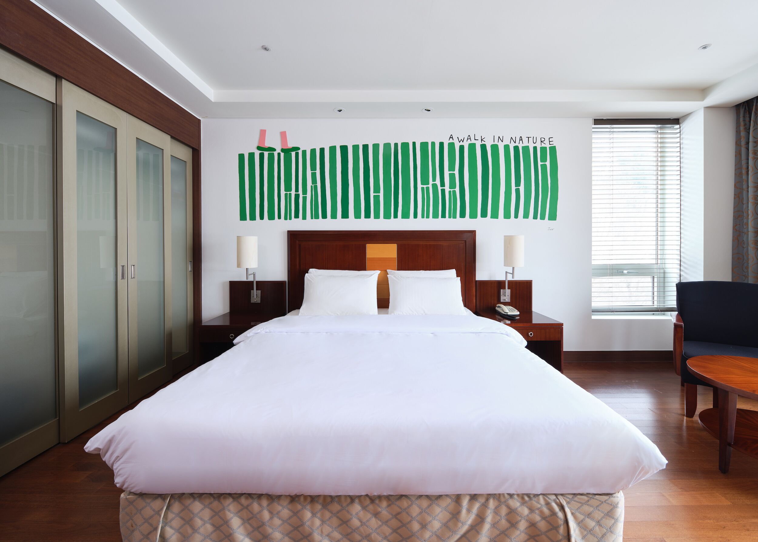 Habitación de hotel con una cama grande, dos mesitas de noche con lámparas, un cabecero de madera, un armario y una ventana con persianas.