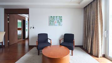 A modern hotel room with two dark armchairs, a wooden coffee table, and a large window with curtains.