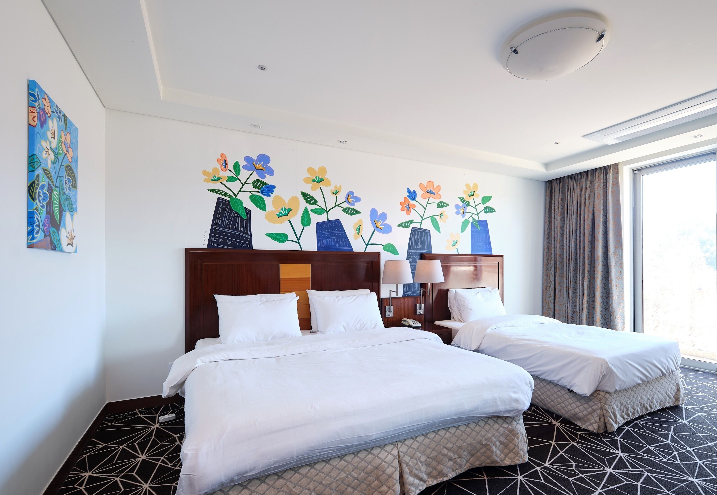 Habitación de hotel con dos camas, un ventanal grande y un mural floral en la pared.