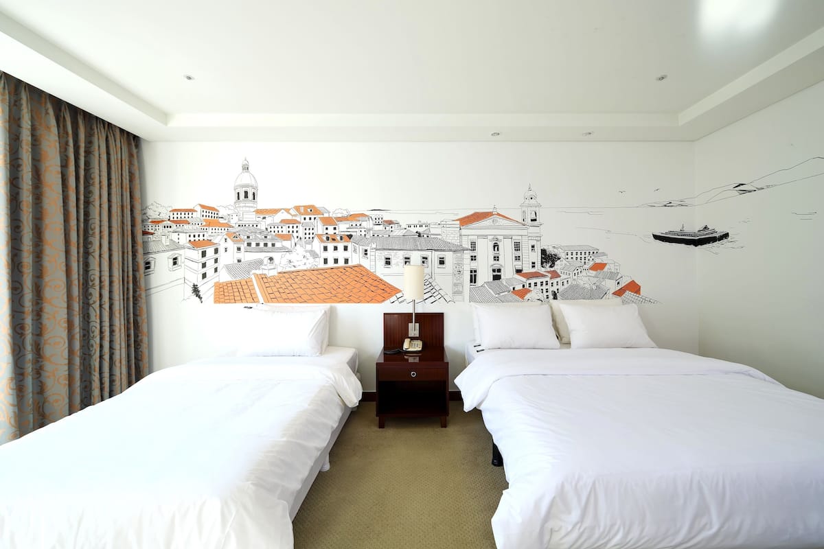 A hotel room with two beds, a nightstand, and a wall mural of a cityscape.