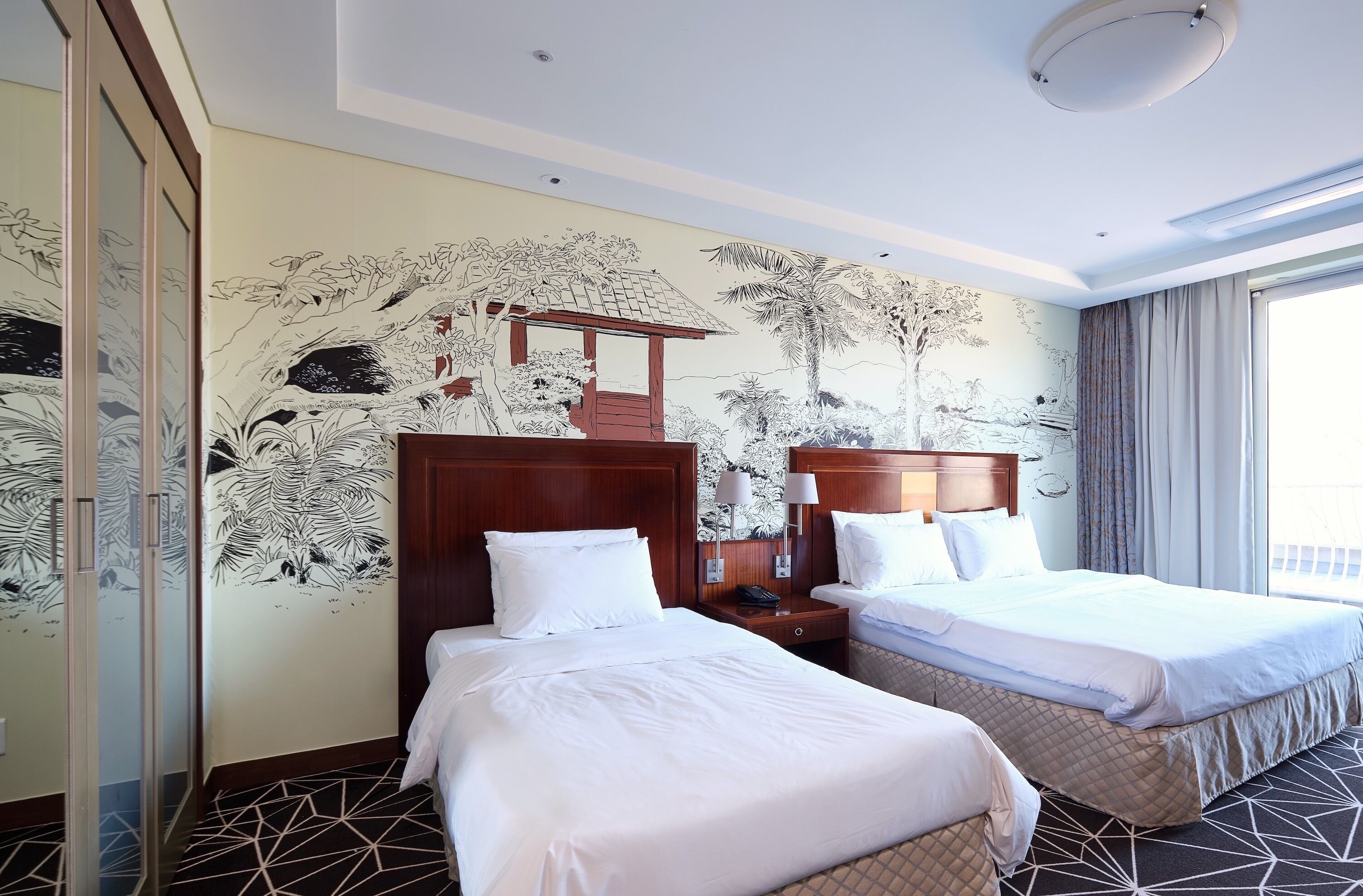 A hotel room with two beds, a large mural on the wall, and a view of the outside.