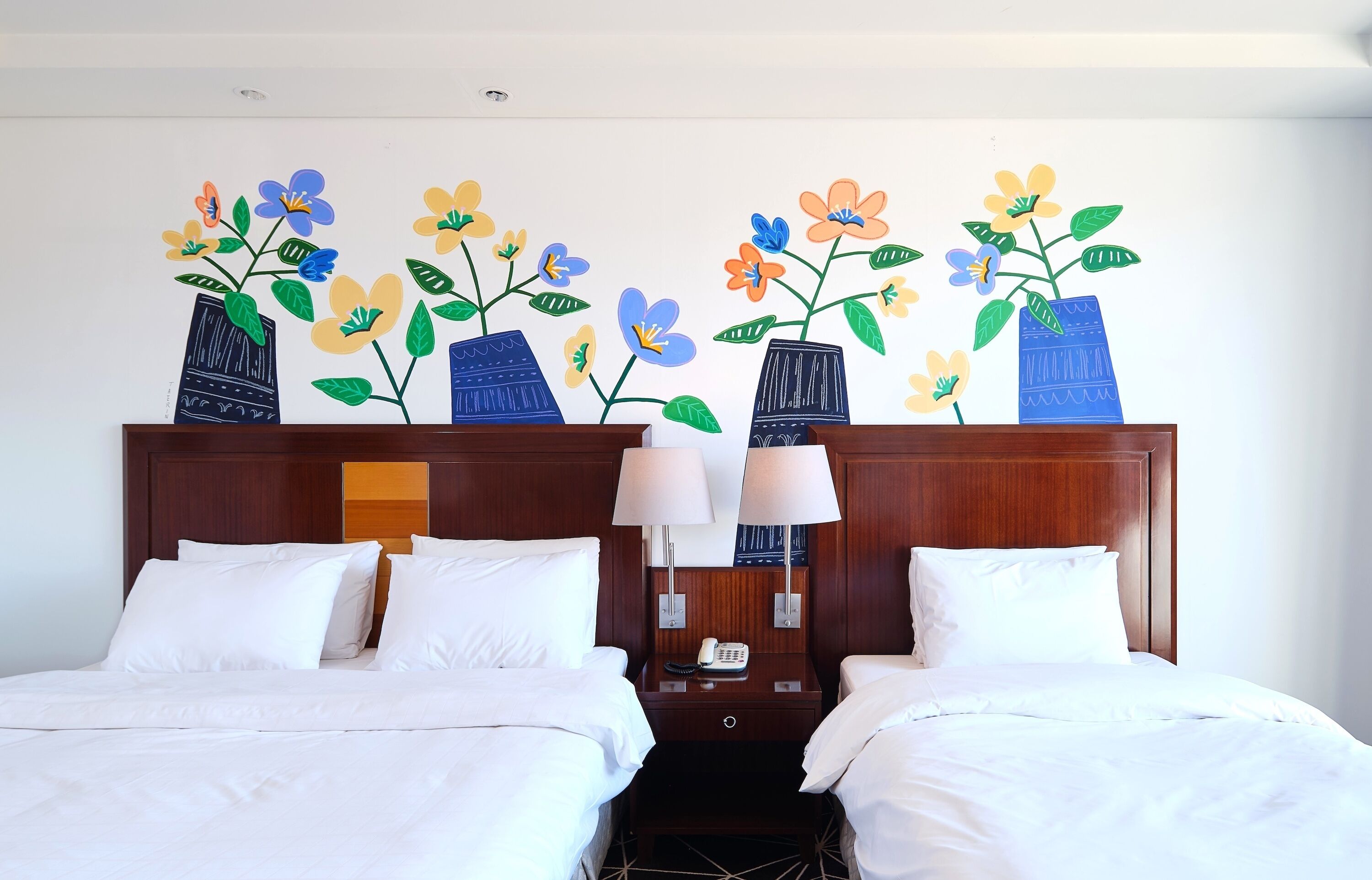 Habitación de hotel con dos camas, cabecero de madera y un mural floral con jarrones.