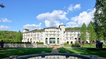 Stately hotel with a central entrance and arched windows, set amidst lush greenery.