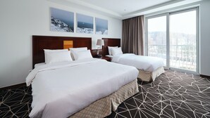 Una habitación de hotel con dos camas, un ventanal con vistas y una alfombra de estampado geométrico.