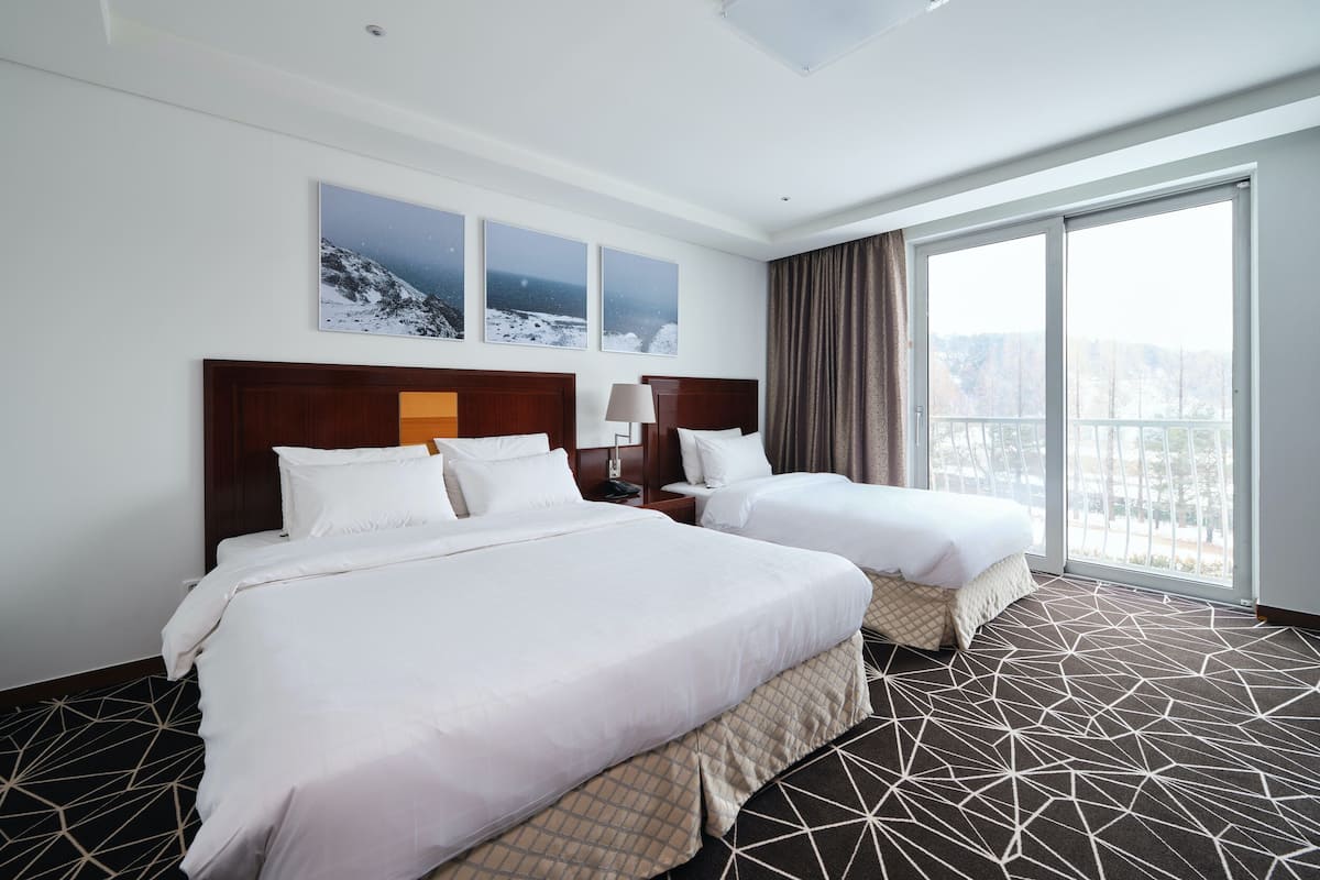 A hotel room with two beds, a large window with a view, and a geometric patterned carpet.