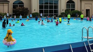 Zona de piscina con varias personas, entre niños y adultos, nadando y conversando.