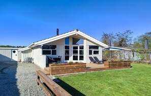 Ein eingeschossiges Gebäude mit geneigtem Dach, großen Fenstern und einer Terrassenfläche mit Sitzgelegenheiten.
