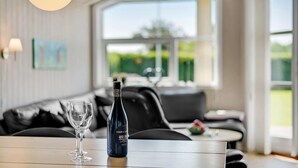 A modern living room with a sofa, a table with a wine bottle and glass, and a large window with a view of greenery. - Cozy home in Haderslev with kitchen (Haderslev)