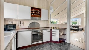 A modern kitchen with white cabinets, a built-in oven, and a microwave. There is a wooden shelf with jars and a window above the sink. - Cozy home in Haderslev with kitchen (Haderslev)