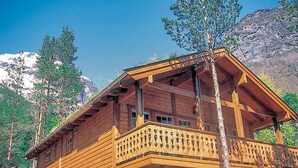 Eine Holzhütte mit Balkon, umgeben von Bäumen und Bergen.