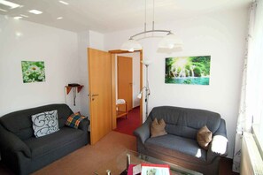 A living room with two grey sofas, a glass coffee table, a wooden door, and two wall-mounted lamps.