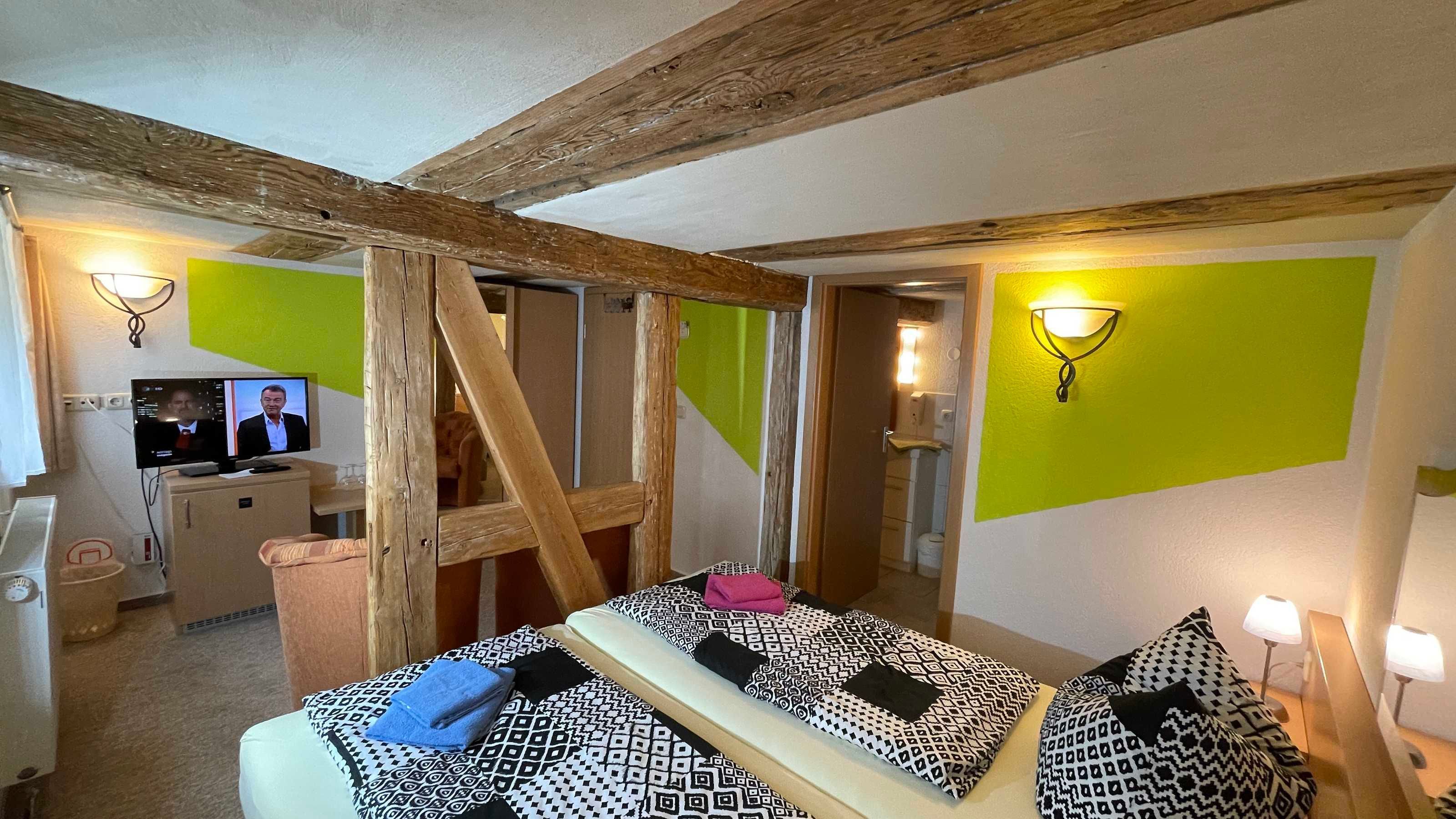 Una habitación con techo de madera, cama con ropa de cama estampada, escritorio con ordenador y pared verde.