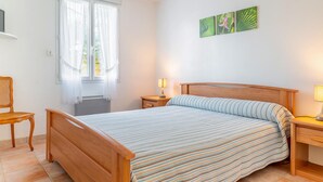Ein Schlafzimmer mit einem hölzernen Bett, zwei Nachttischlampen, einem Sessel und einem Fenster mit durchsichtigen Vorhängen.