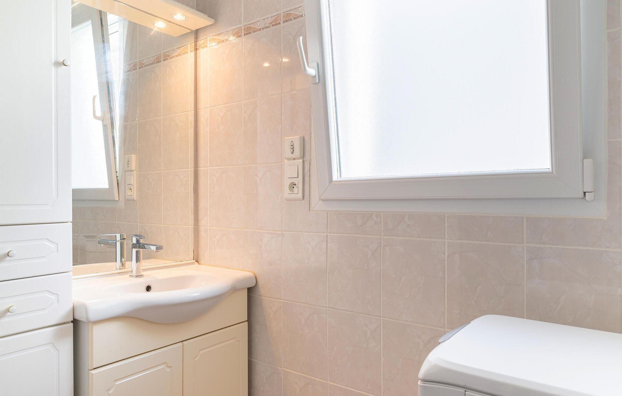 Un baño con lavamanos blanco, espejo y ventana.