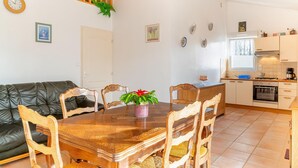 Ein gemütliches Wohnzimmer mit einem Holzespeisetisch, Stühlen und einem schwarzen Ledersofa. Im Hintergrund ist eine Küche mit modernen Geräten und einem Fenster zu sehen.