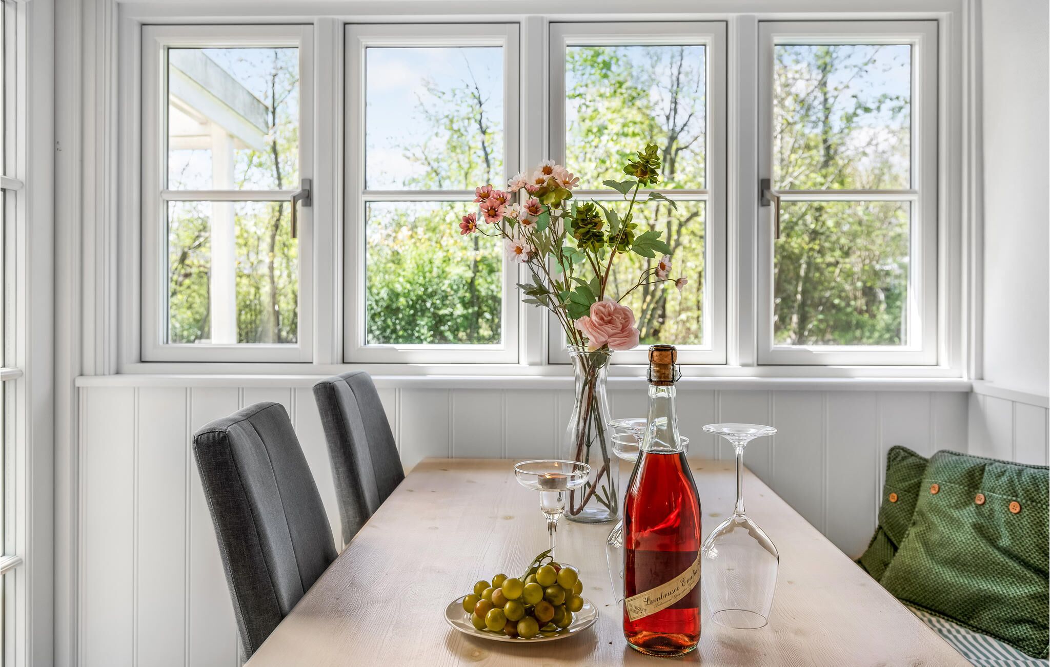 A dining table with a vase of flowers, a bottle of wine, and a plate of grapes.