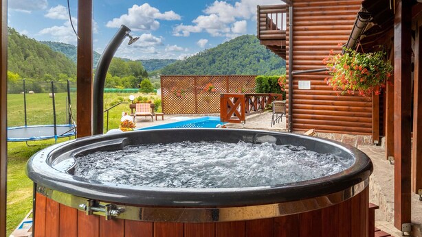 Un jacuzzi con revestimiento de madera, vistas a un paisaje montañoso y una piscina al fondo.
