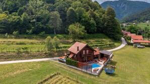 Una cabaña de madera con piscina, rodeada de exuberante vegetación y montañas al fondo.