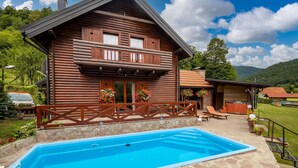 Una cabaña de madera con balcón, piscina y zona de patio con mobiliario exterior.