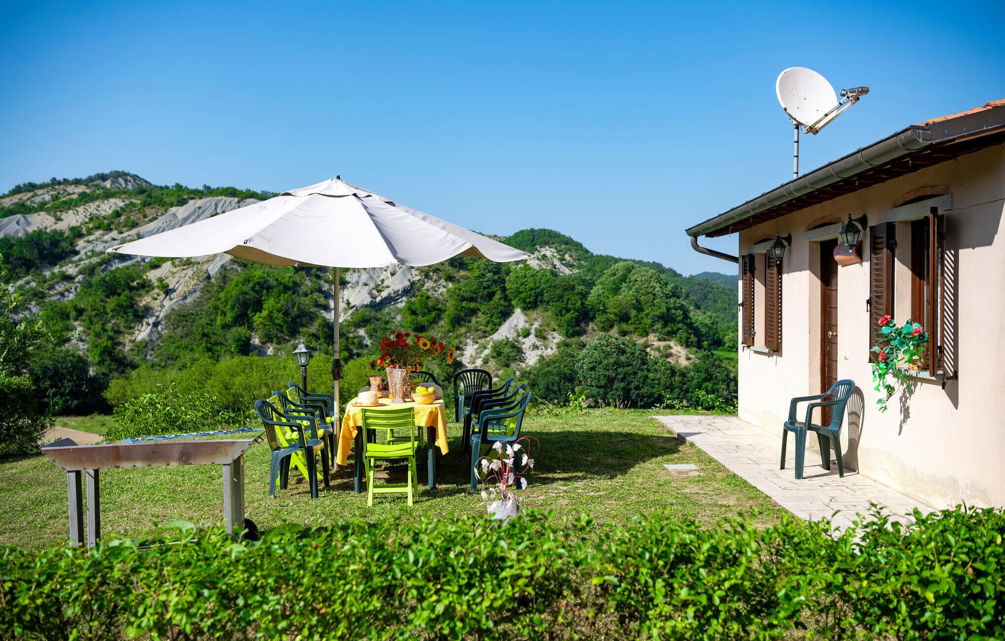 Un espace de restauration en plein air avec une table et des chaises, un parasol blanc et une vue sur les montagnes en arrière-plan.