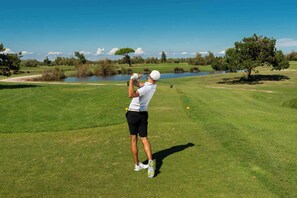 A person playing golf on a well-maintained course with a water body in the background. - Holiday Home with Pool and Terrace (Albarella)