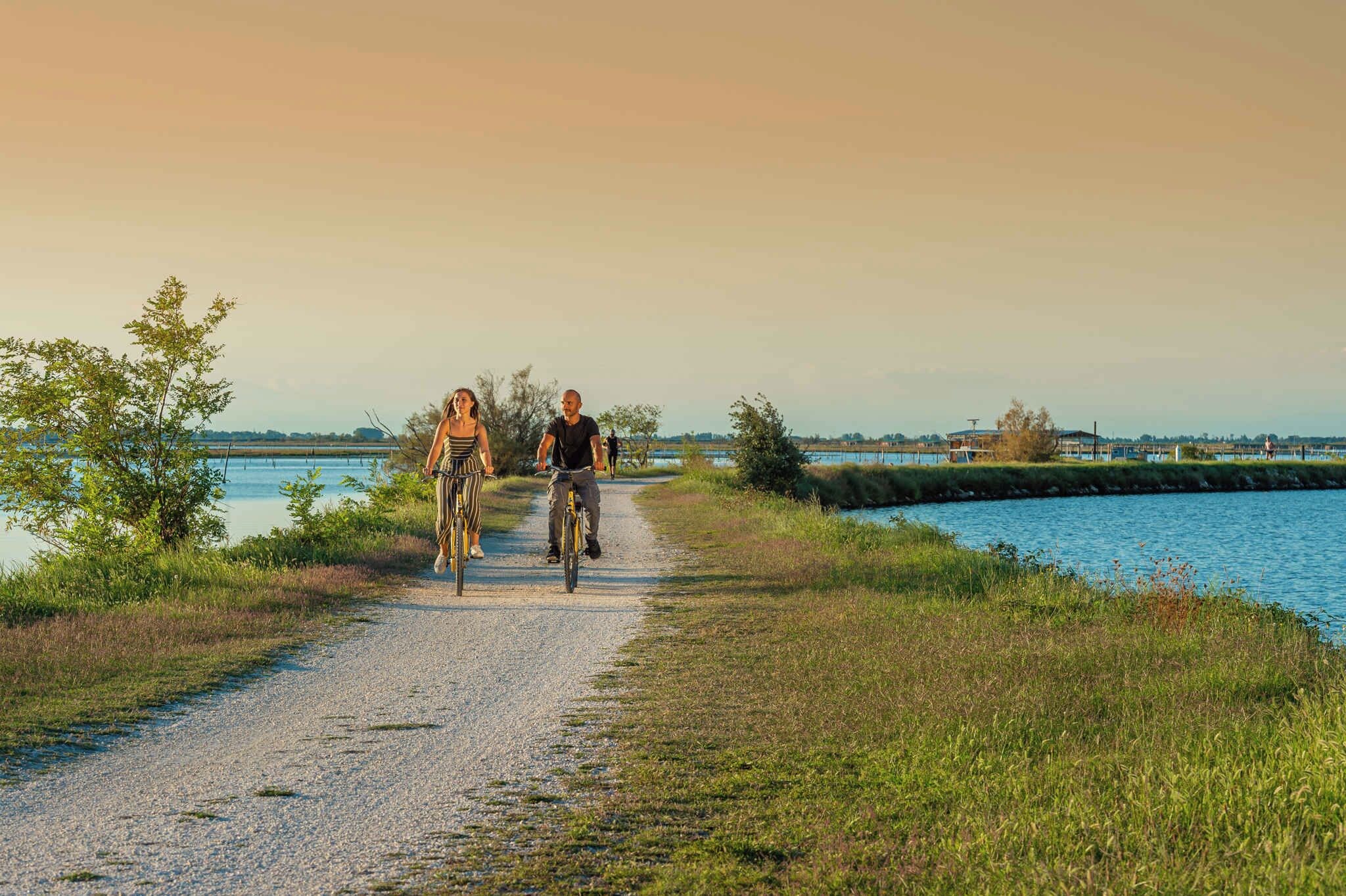 A gravel path alongside a body of water with trees and a distant building.