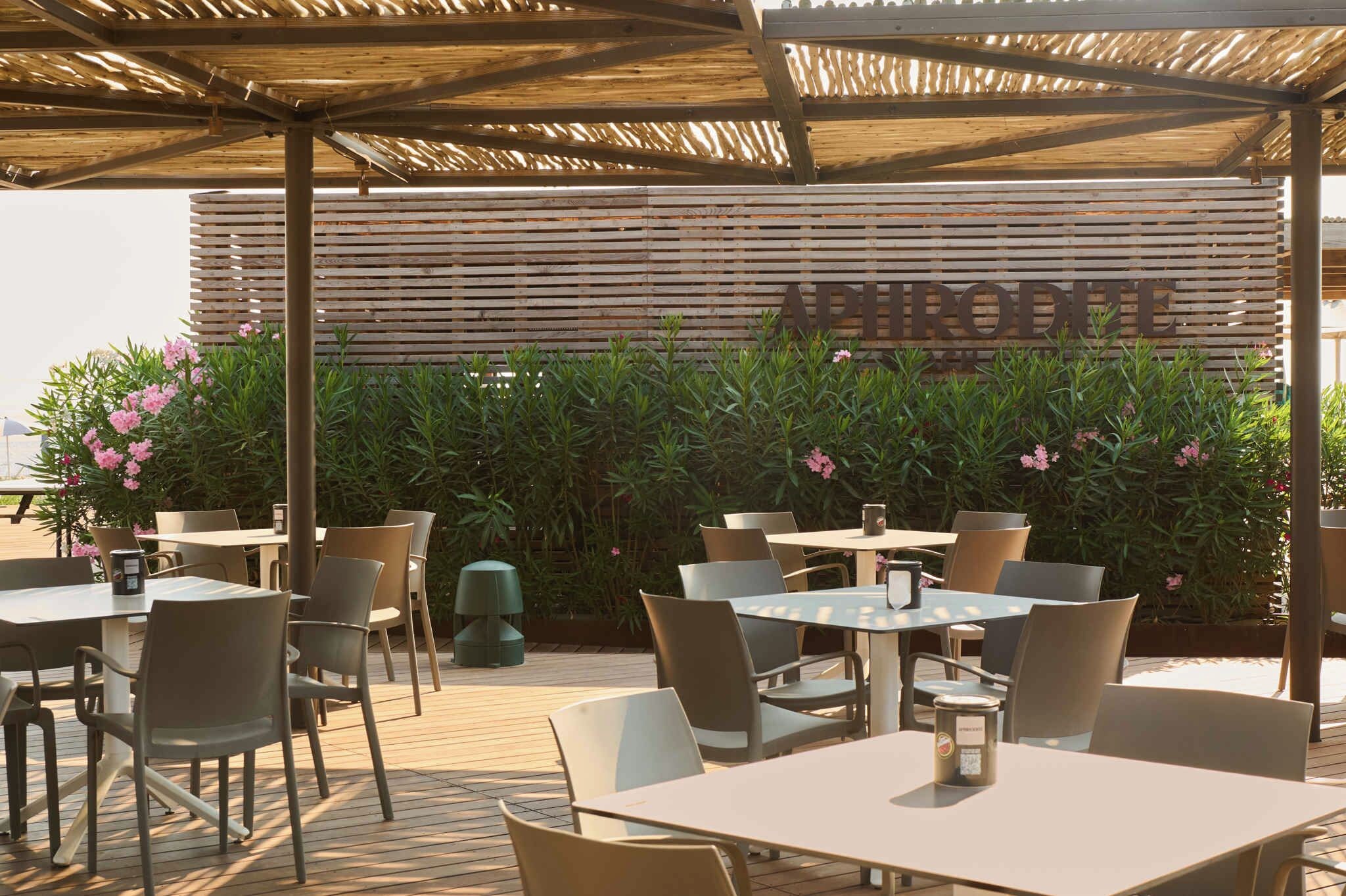 Een terras met tafels en stoelen, een houten pergola en een achtergrond met een bord.