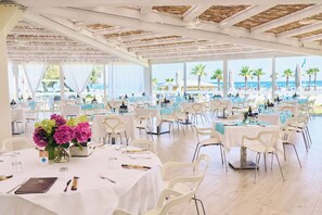 A spacious outdoor dining area with multiple tables and chairs, overlooking a beach with palm trees and the sea. - Holiday Home with Pool and Terrace (Albarella)