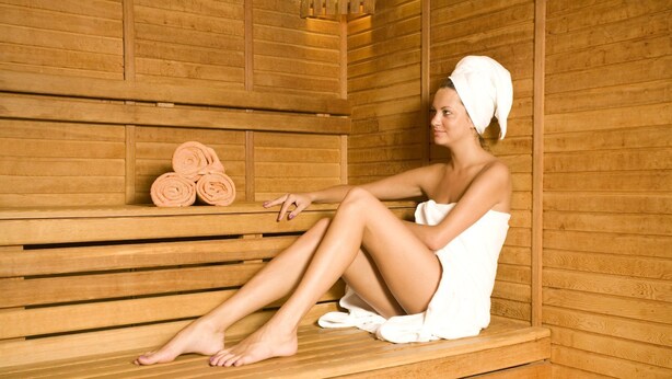 Una persona sentada en una sauna de madera con toallas y toallas enrolladas en un estante.