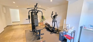 Un espace dédié à la remise en forme, équipé d’un banc de développé couché, d’une machine à câbles et d’un vélo d’appartement.