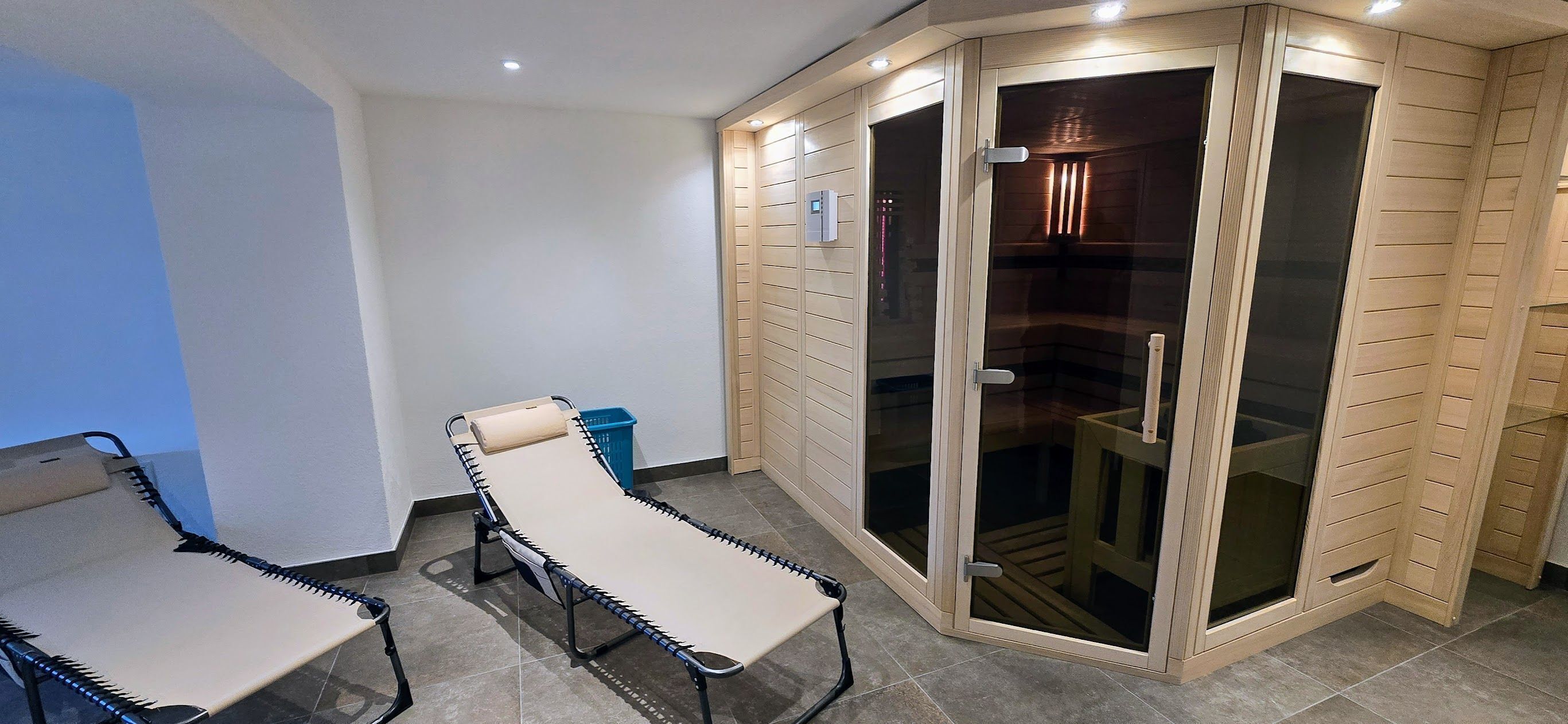 Una habitación con camilla de masaje, una banqueta pequeña y una puerta corredera de vidrio que da a una zona de ducha.
