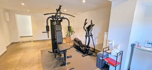 Een sportschool met trainingsapparatuur, een prullenbak en een kleine tafel met een rode stoel.