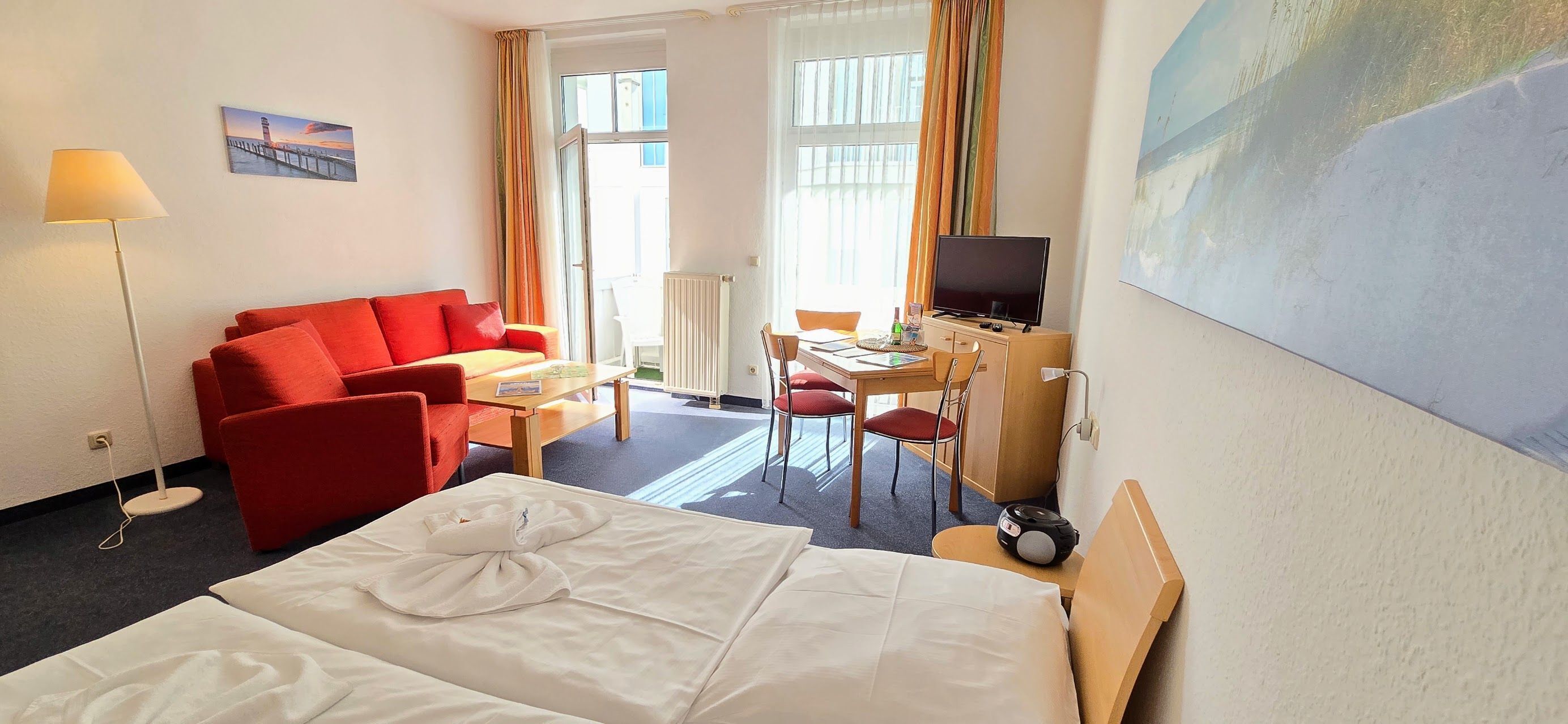 Een hotelkamer met een bed, een rode bank, een bureau met een televisie en een schilderij aan de muur.