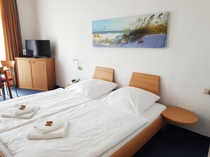 Een hotelkamer met een bed, een televisie, een bureau en een schilderij van een strand.