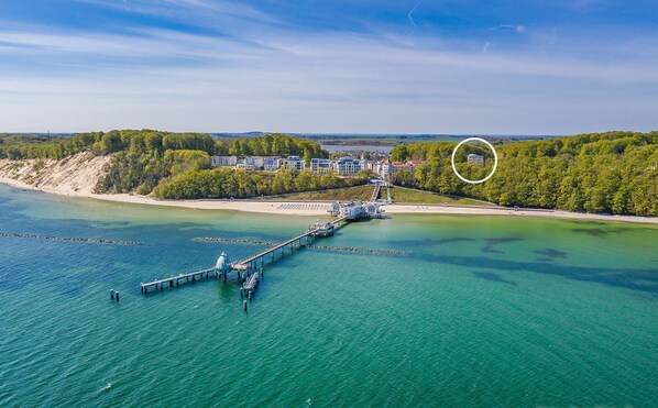 Ein Luftbild einer Küstenregion mit einem Steg, der sich ins Wasser erstreckt, umgeben von Gebäuden und Grünflächen.
