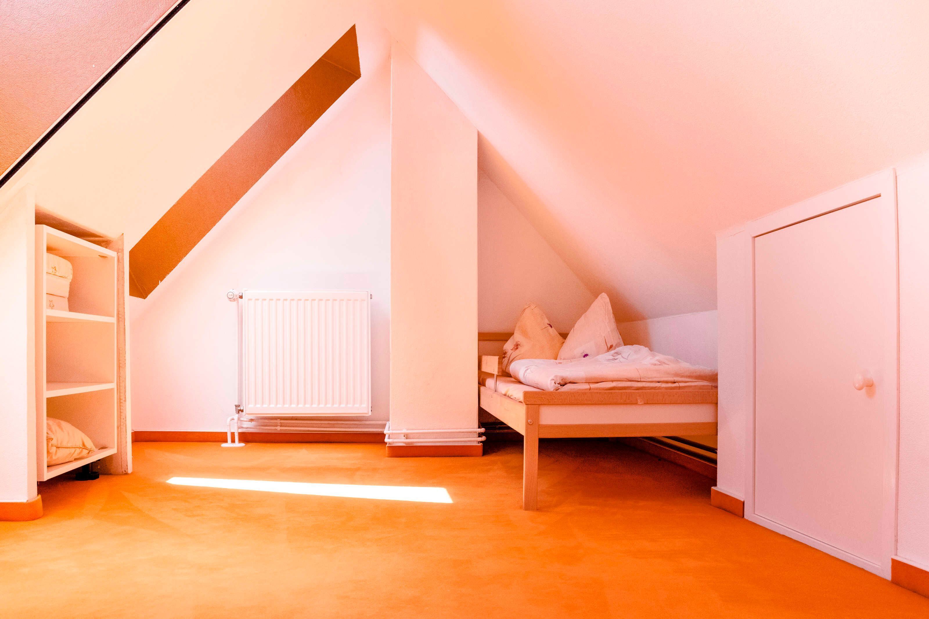 A bedroom with a sloped ceiling, a radiator, a bed with pillows, a wardrobe, and a shelf unit.