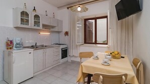 Une cuisine compacte avec un coin repas, un téléviseur fixé au mur et une fenêtre avec des rideaux.