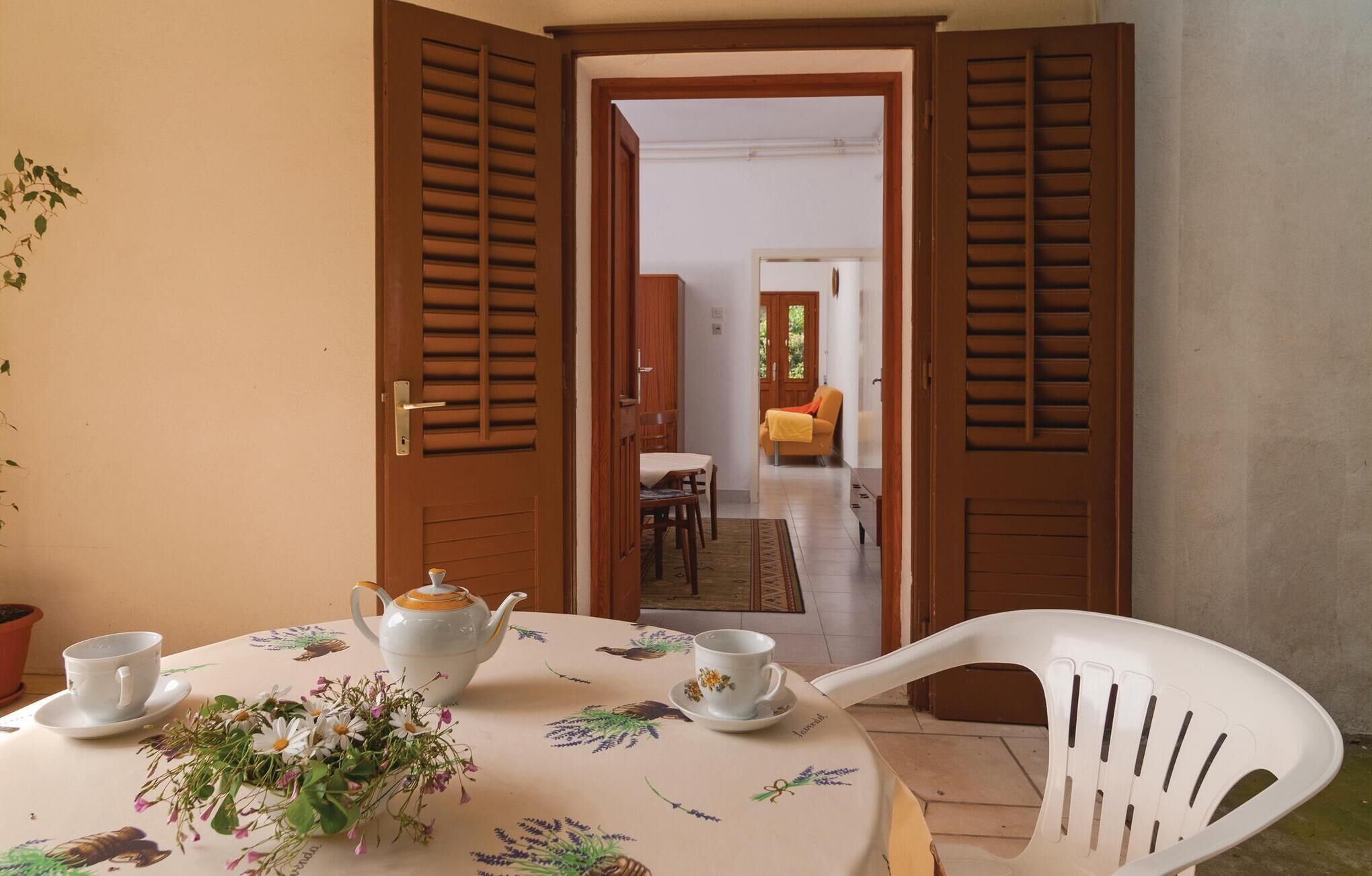 A dining area with a table set for two, a white teapot, two cups, and a floral arrangement.