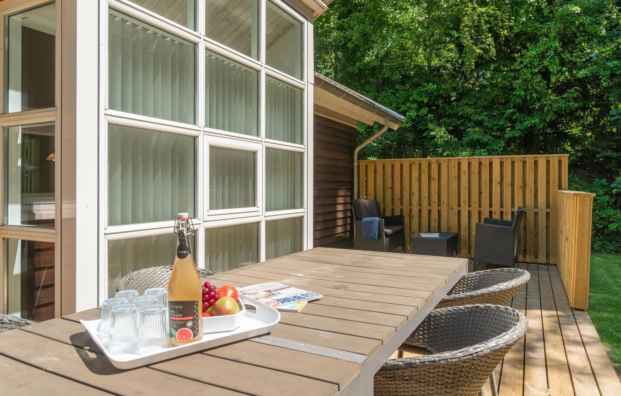 A wooden deck with a table set for a meal, a bottle of lemonade, and a tray of glasses.
