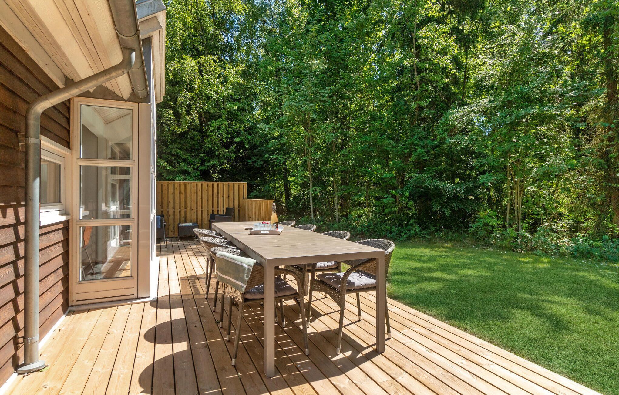 Une terrasse avec une table et des chaises, une clôture en bois et un jardin luxuriant.