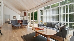 A modern living room with a wooden ceiling, a grey sofa, two armchairs, a coffee table, and a view of a garden through large windows. - Stunning home in Hasle with sauna (Hasle)