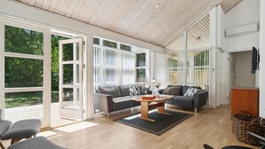 A spacious living room with a large sliding glass door leading to a deck, a grey sofa set, a wooden coffee table, and a wicker basket. - Stunning home in Hasle with sauna (Hasle)