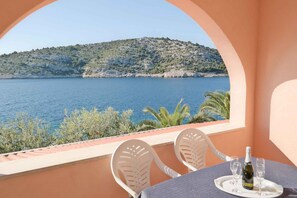 A balcony with a table set for two, overlooking a body of water and a hilly landscape.